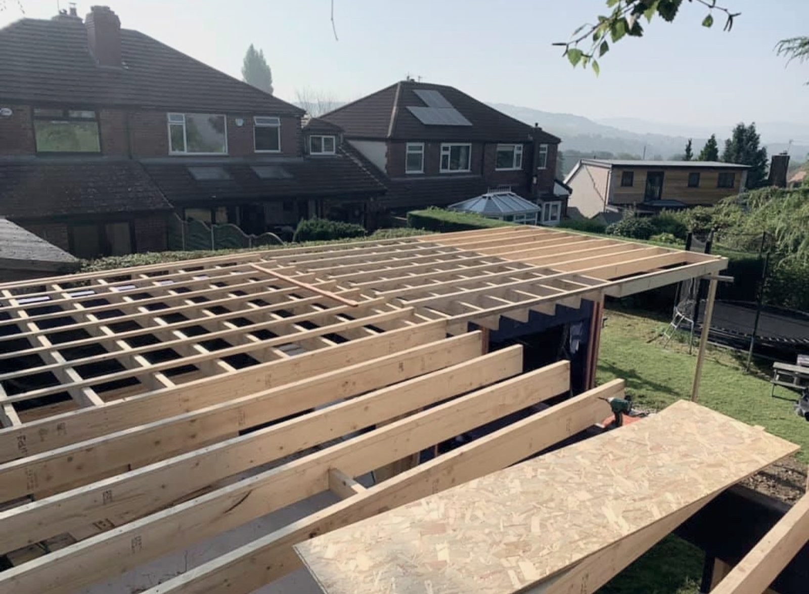 The timber frame for a new flat roof going up, with the first sheet of decking laid on the joists