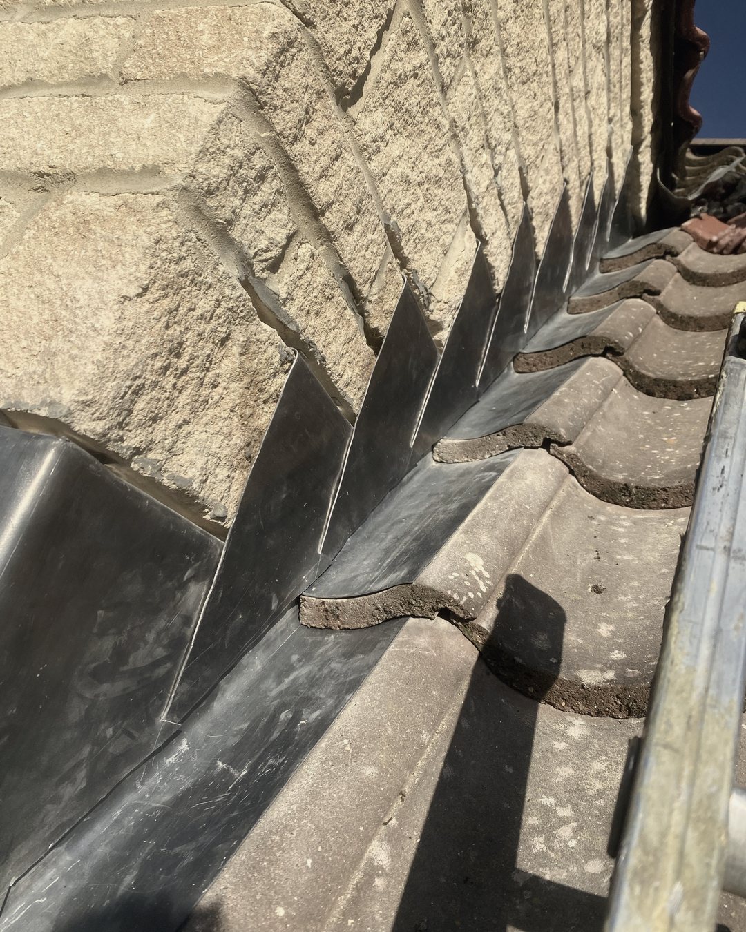 New lead step flashing cut into the joints of a stone wall and dressed over the roof tiles
