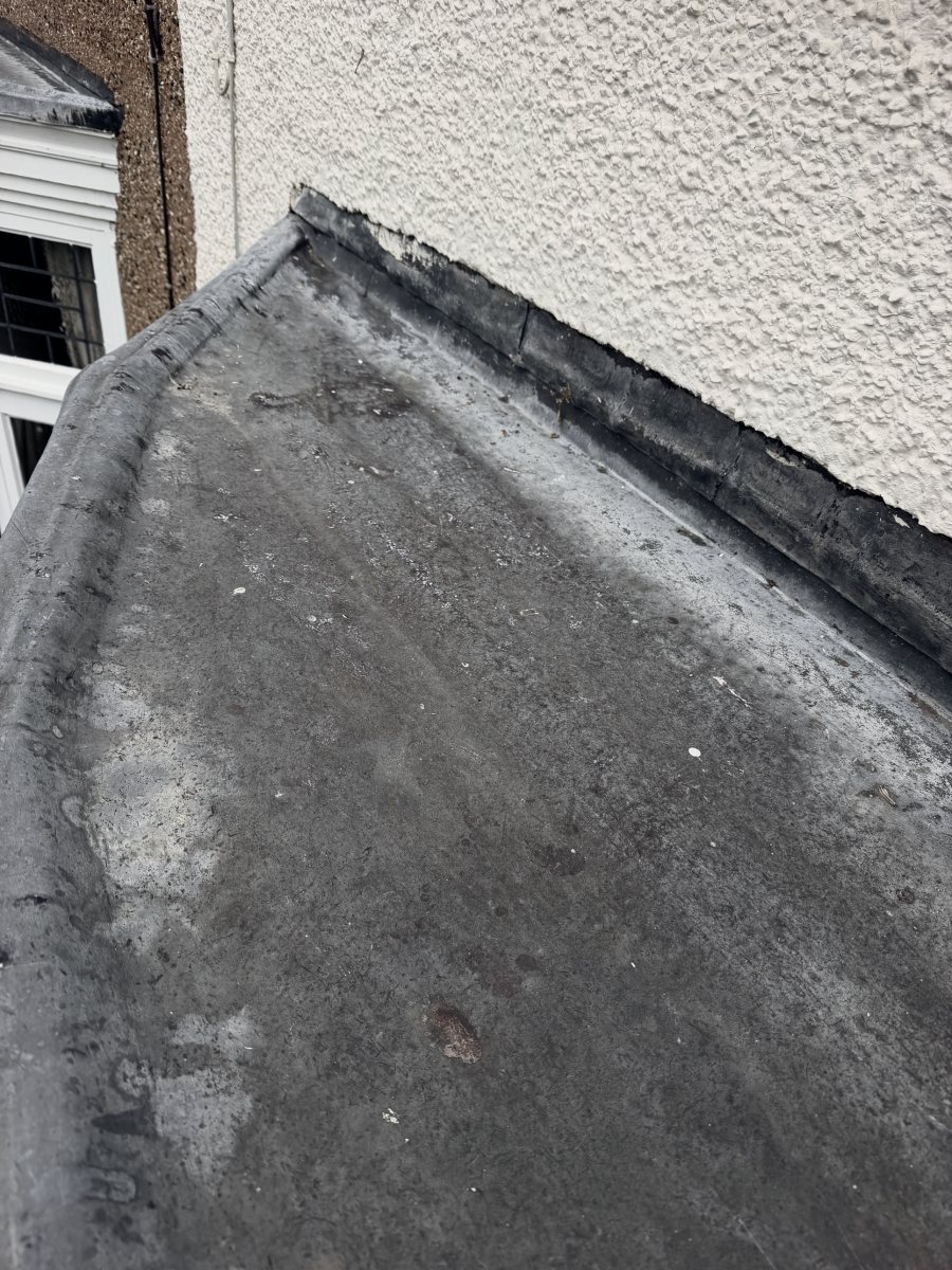 Close-up of the old lead, worn and stained, turned up against the rendered wall
