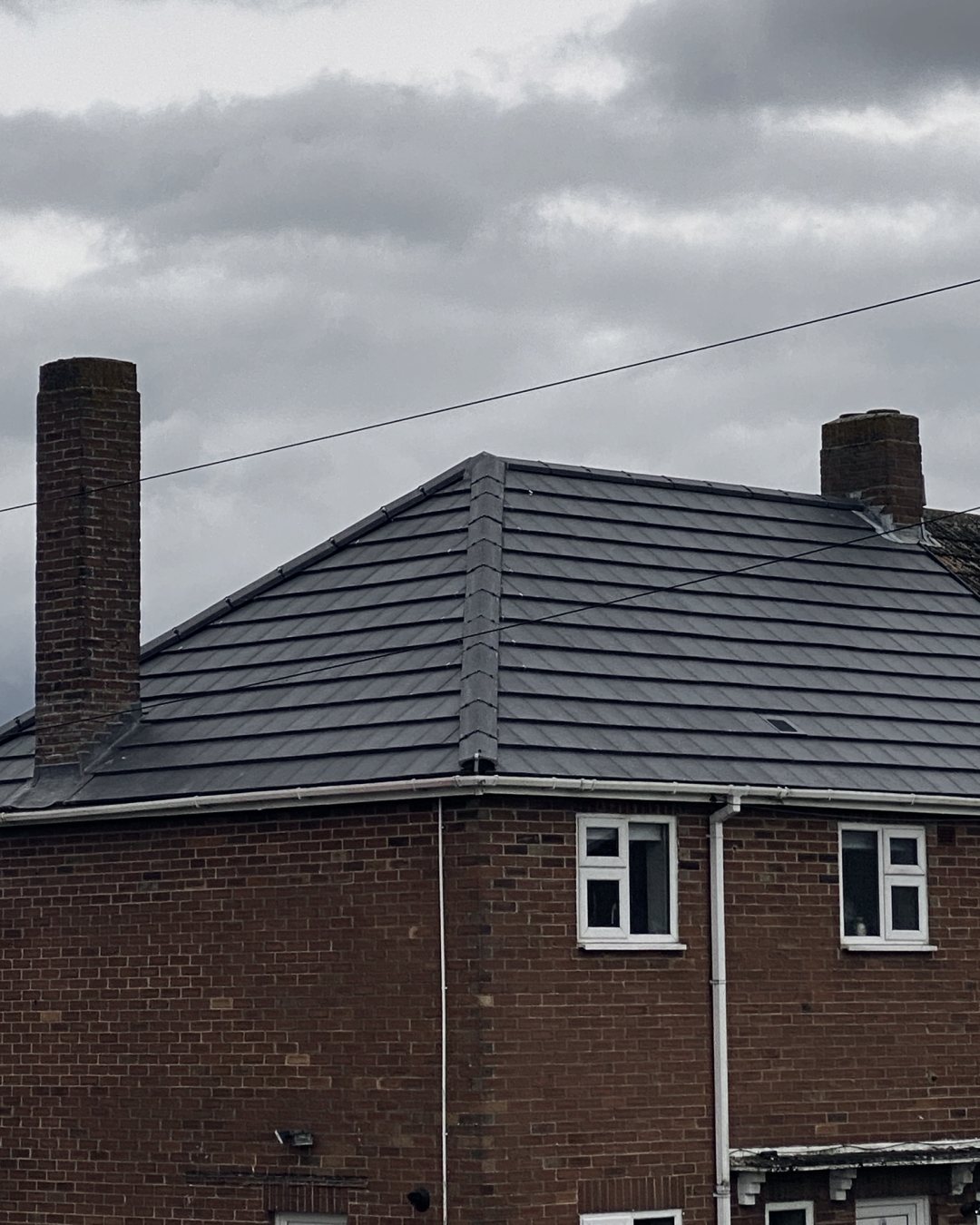 The re-tiled grey hipped roof on a red-brick semi, next to the neighbour's old brown tiled roof