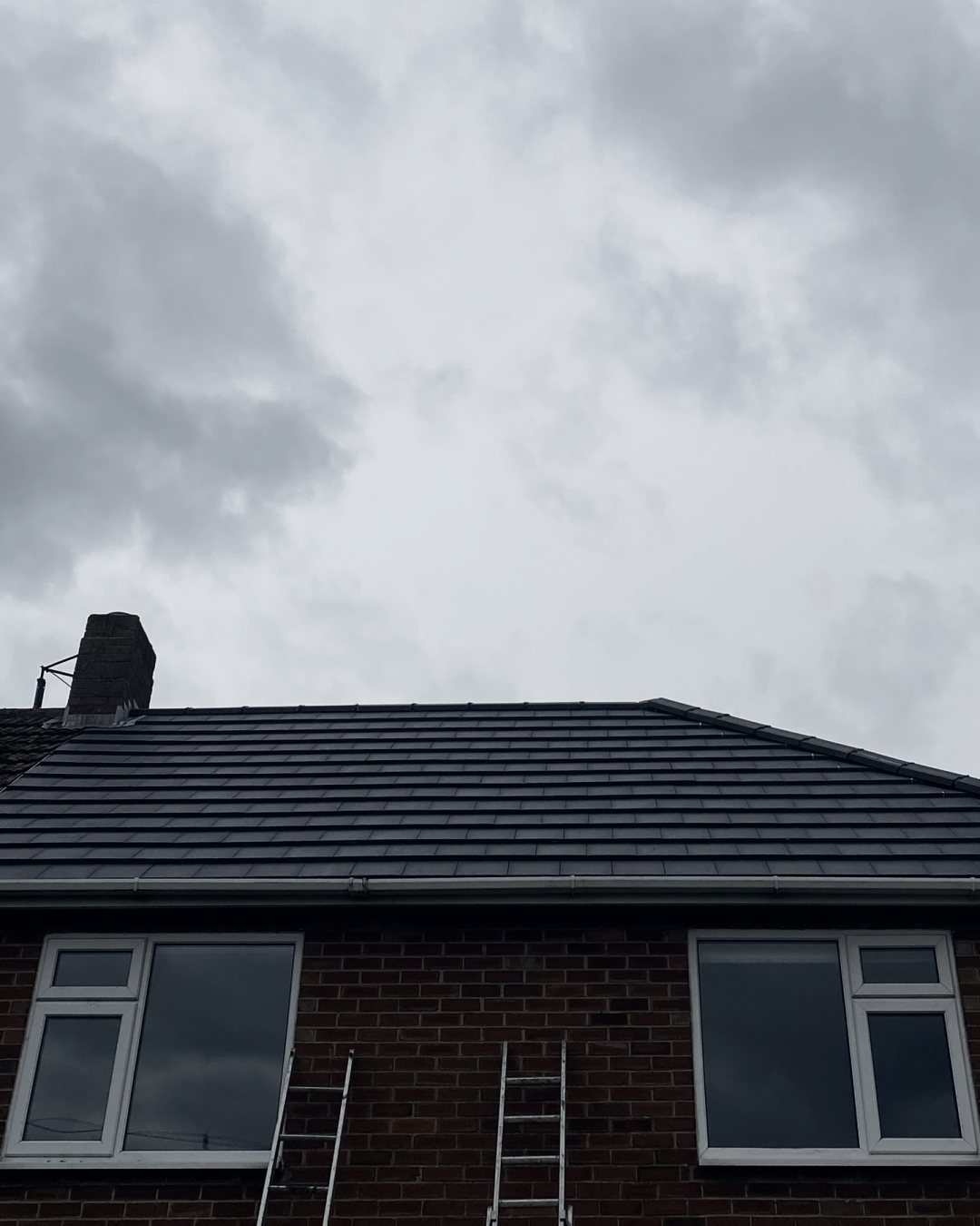 The front slope of the new grey roof, with two ladders against the wall below